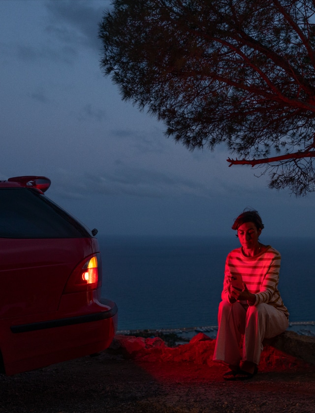 Person sitting next to car using Emergency SOS safety feature from an iPhone 15
